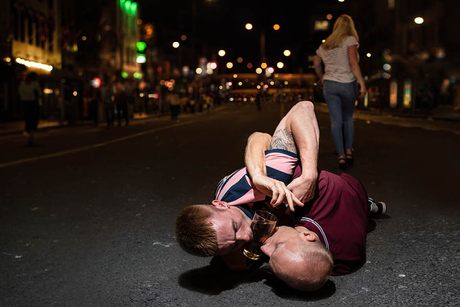 Two men on the ground wrestling over beer