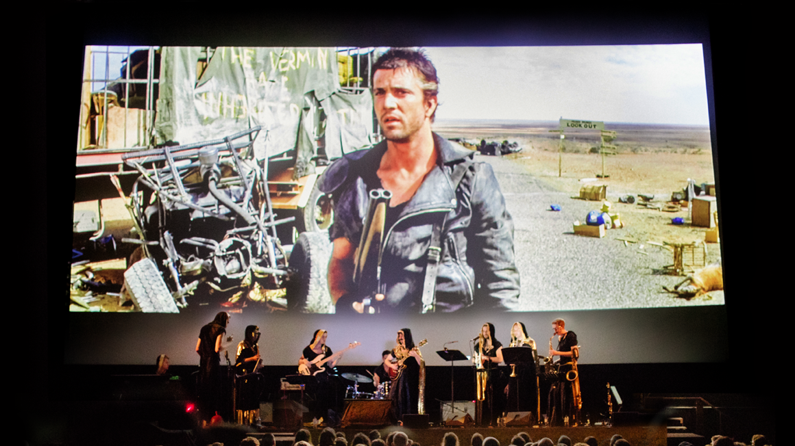 Mad Max playing on screen with live band on stage