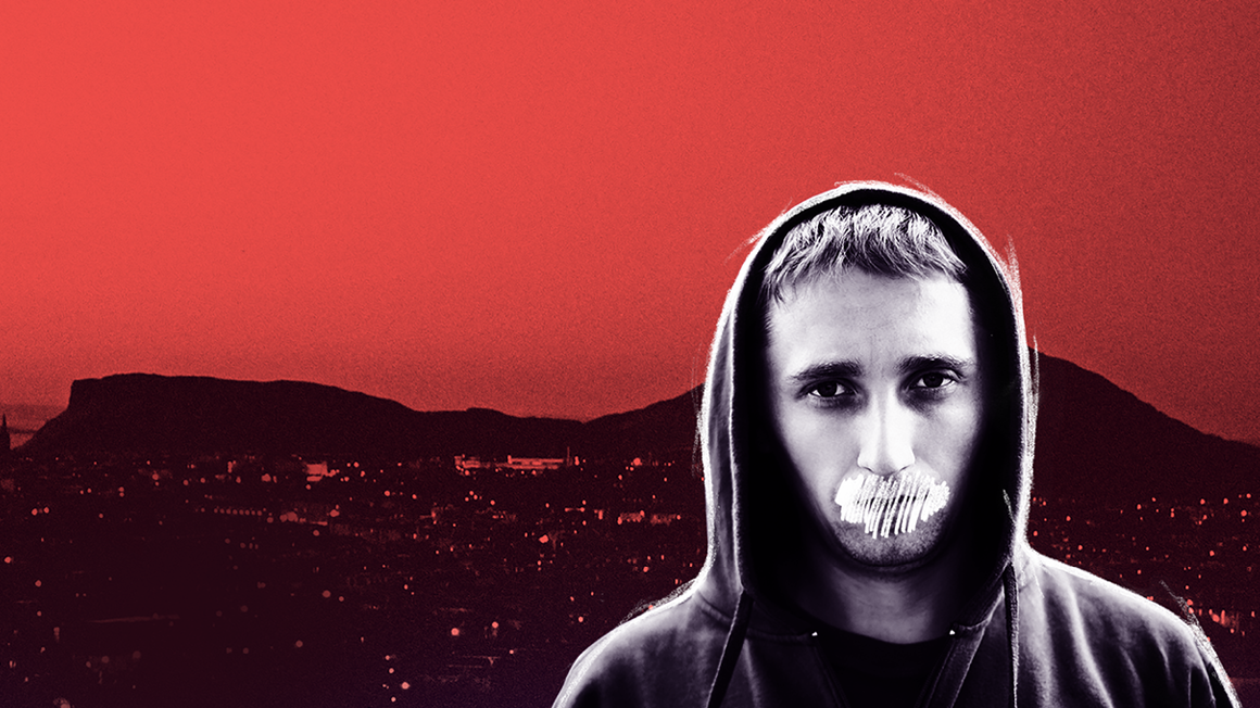 Young man stands in front of hills to the distance with mouth scribbled out